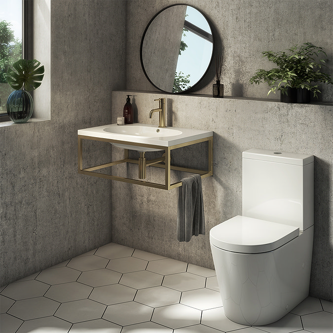 Minimalist bathroom with floating brass vanity unit, white sink, round mirror, and modern toilet on hexagonal floor tiles