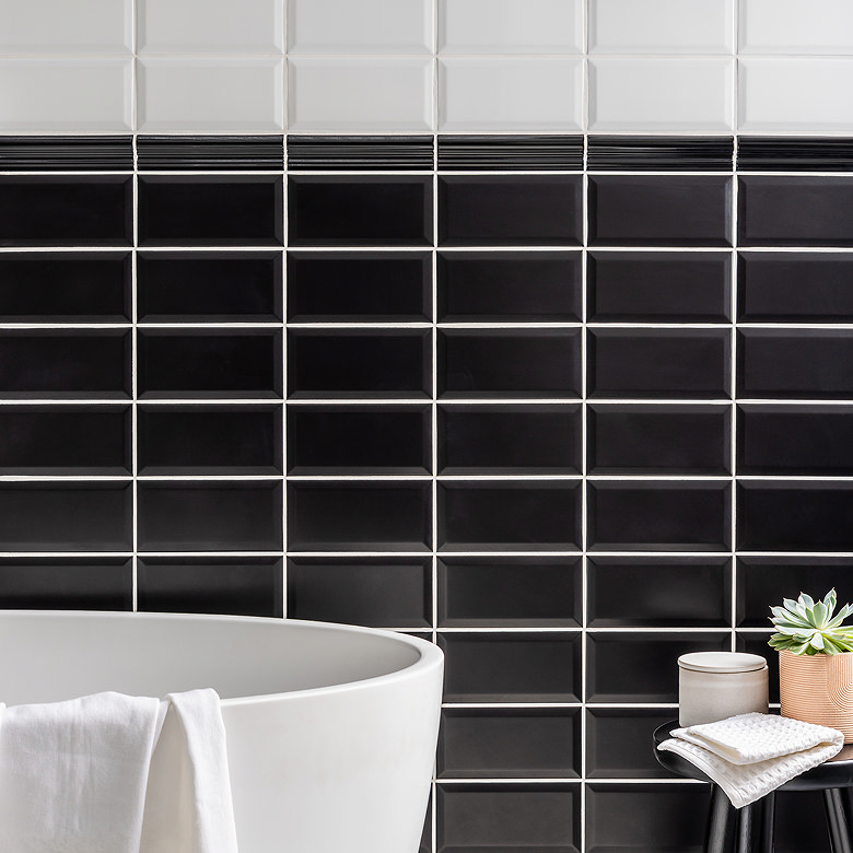 Black and white bevelled metro tiles behind a freestanding white bath.