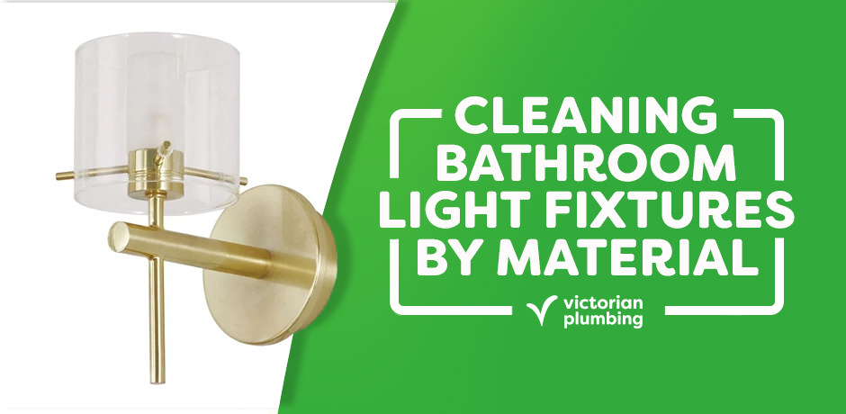 Brushed brass bathroom wall light with clear cylindrical glass shade next to a green banner reading “Cleaning Bathroom Light Fixtures by Material” from Victorian Plumbing.