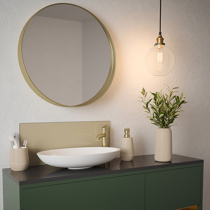 Stylish bathroom vanity with round mirror, pendant light, and green cabinet, featuring a white vessel sink and gold faucet, complemented by beige accessories and a potted plant.