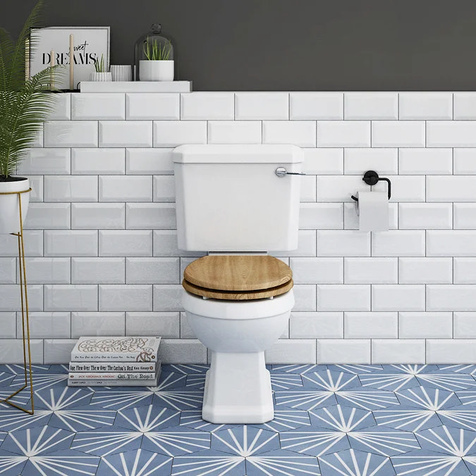 White toilet with wooden seat, white subway tiles, and blue patterned floor