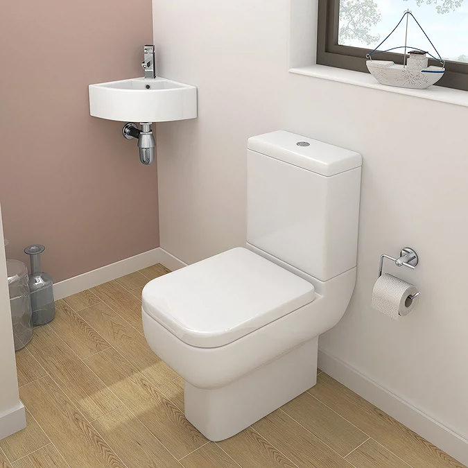 Small cloakroom with white corner wall-hung basin and close-coupled toilet on wood-effect flooring.