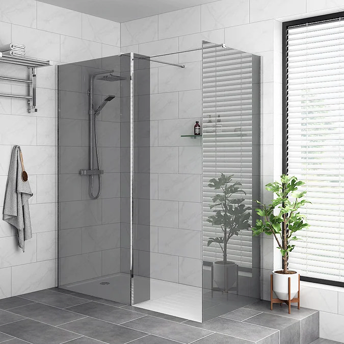 Minimalist wet room with a sleek walk-in shower, featuring a chrome rainfall showerhead and glass screen. White marble-effect tiles on the walls complement grey floor tiles, creating a modern, clean aesthetic. A potted plant and towel rack add a touch of warmth and practicality.