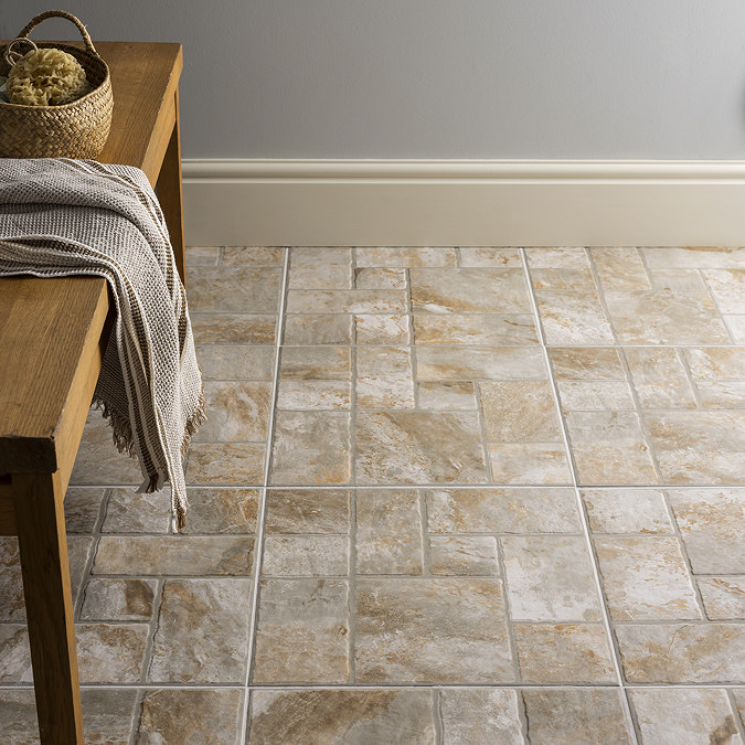 Rustic stone-effect ceramic floor tiles in a neutral colour palette, arranged in a geometric pattern. The textured surface adds warmth and character, enhancing the cosy, natural vibe of the space, complemented by a wooden bench with a woven basket and blanket.