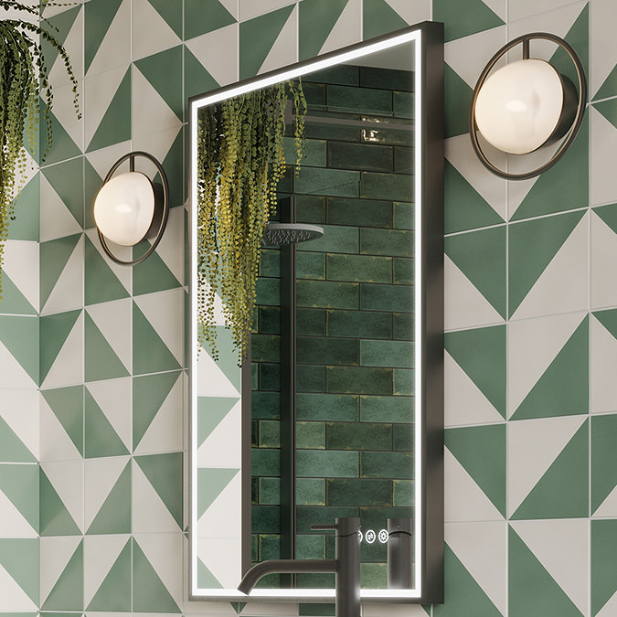 Modern bathroom design showcasing a rectangular LED-illuminated mirror framed by geometric green and white tiles, accented with brass wall lights and greenery, reflecting a green tiled shower area.