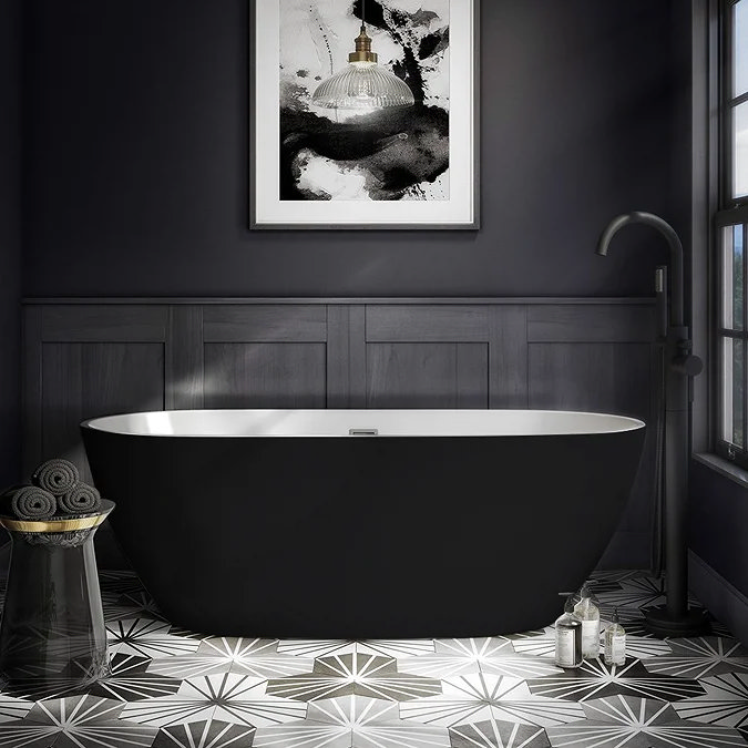 Luxurious black freestanding bathtub in a boutique-style bathroom featuring deep charcoal tones, geometric patterned tiles, a modern black floor-standing tap, and framed monochrome artwork.