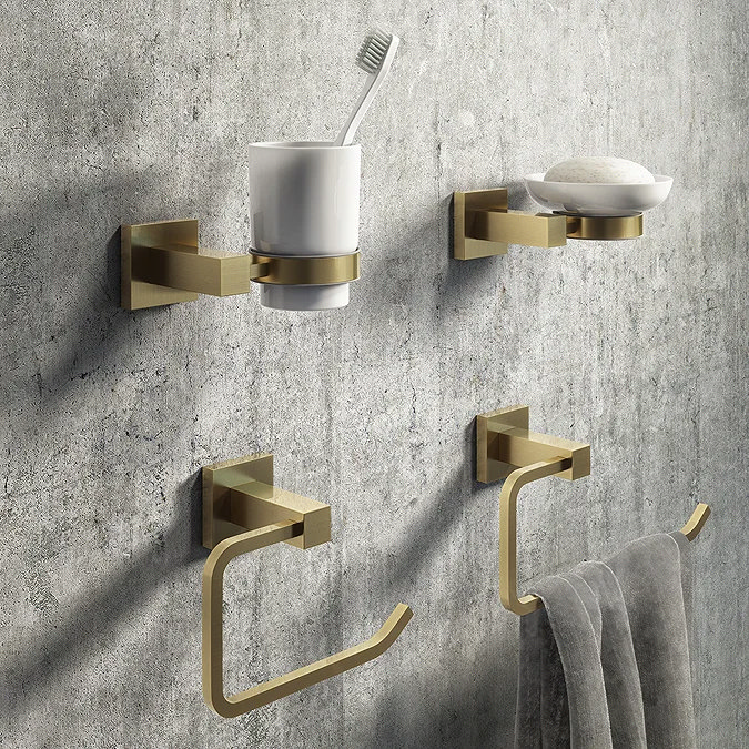 Brushed brass bathroom accessory set including toothbrush holder, soap dish, towel ring, and toilet paper holder mounted on a textured grey wall, adding a touch of modern luxury to the bathroom.