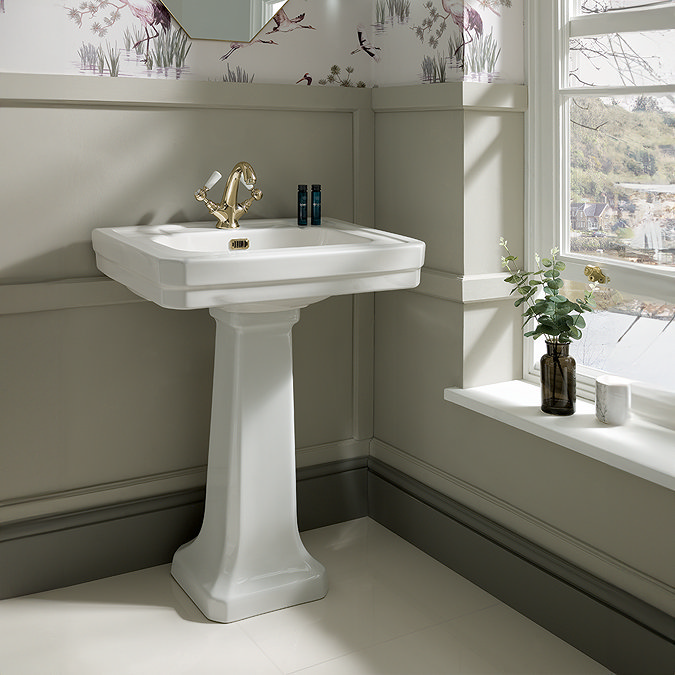 Classic white pedestal sink with gold taps in a light-filled traditional bathroom with nature-themed wallpaper