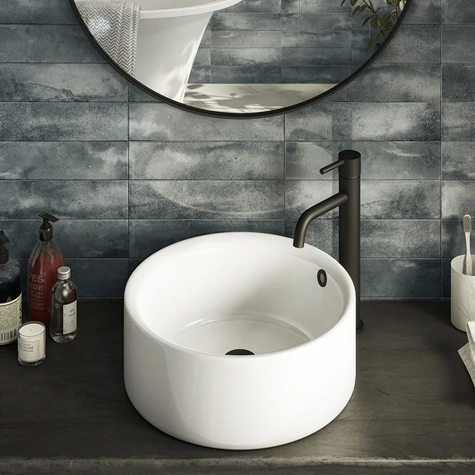 White round countertop basin with matt black tap on a dark vanity unit.