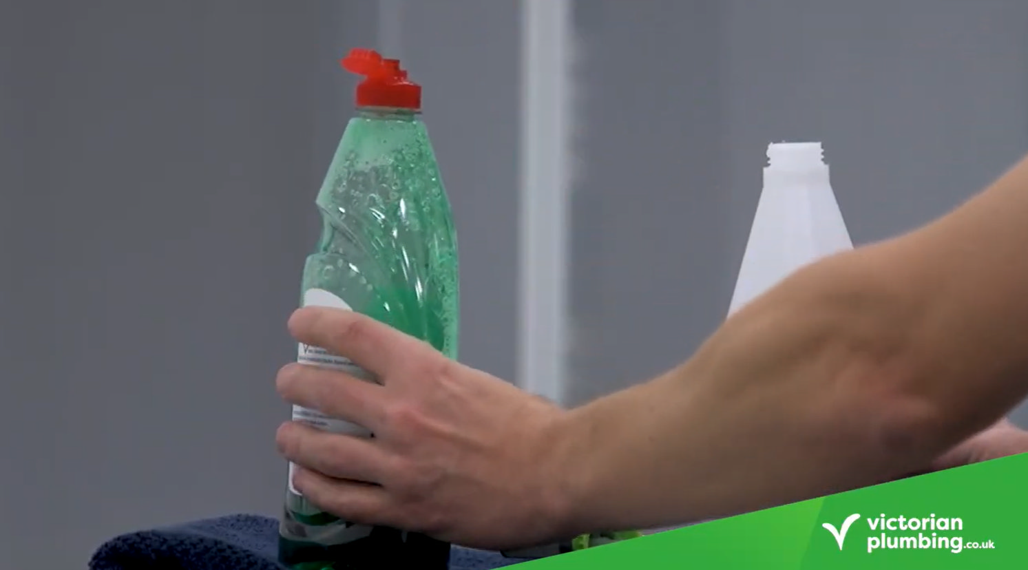 Hand holding a bottle of washing-up liquid, preparing a mild cleaning solution for bathroom wall panels.