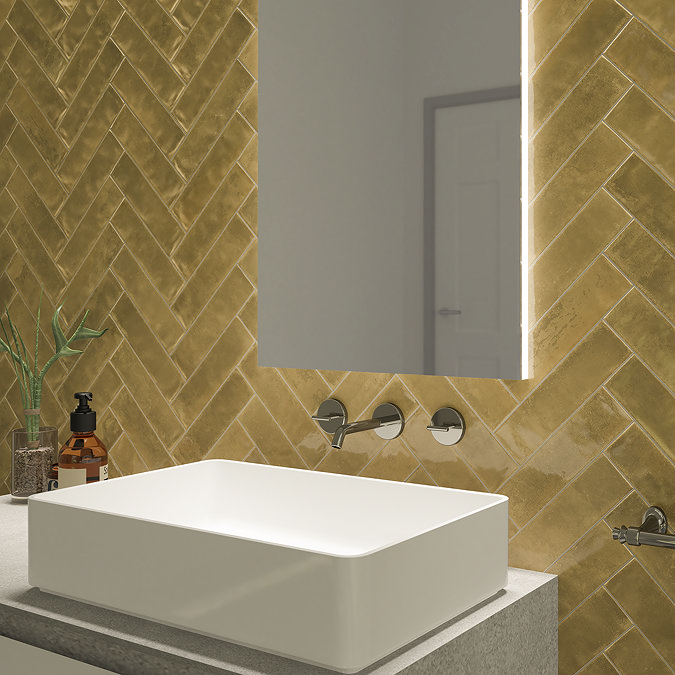 Modern bathroom with gold herringbone tiles, a wall-mounted square sink, and an illuminated mirror above. Sleek silver faucets and a potted plant add stylish accents to the vanity area.