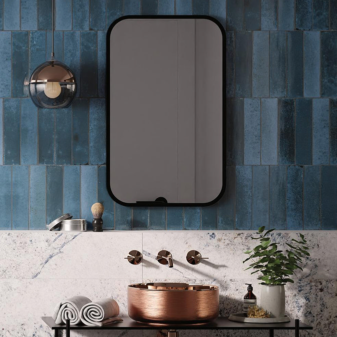 Contemporary bathroom with bold blue feature tiles, a copper vessel sink, wall-mounted brass taps, and a black-framed mirror against marble-effect surfaces.