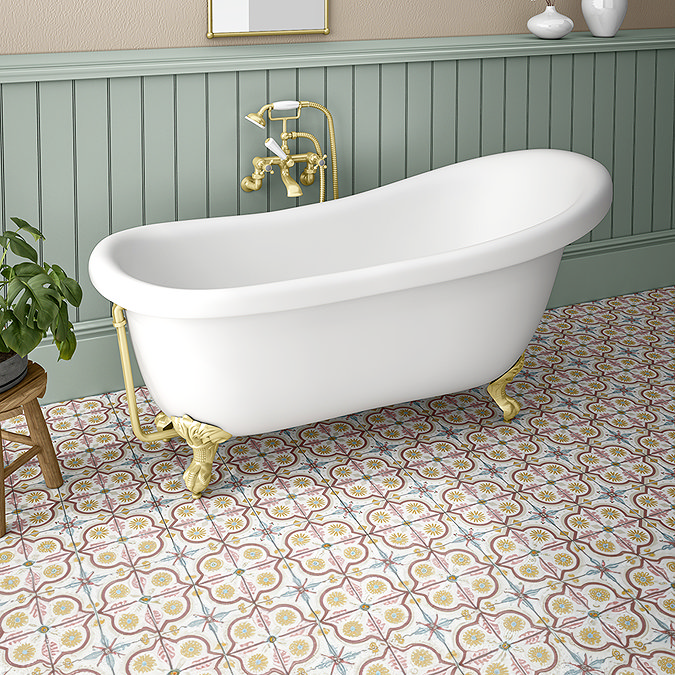 Freestanding white clawfoot bathtub with brass fixtures set against sage green wall panelling and vintage-inspired patterned floor tiles.