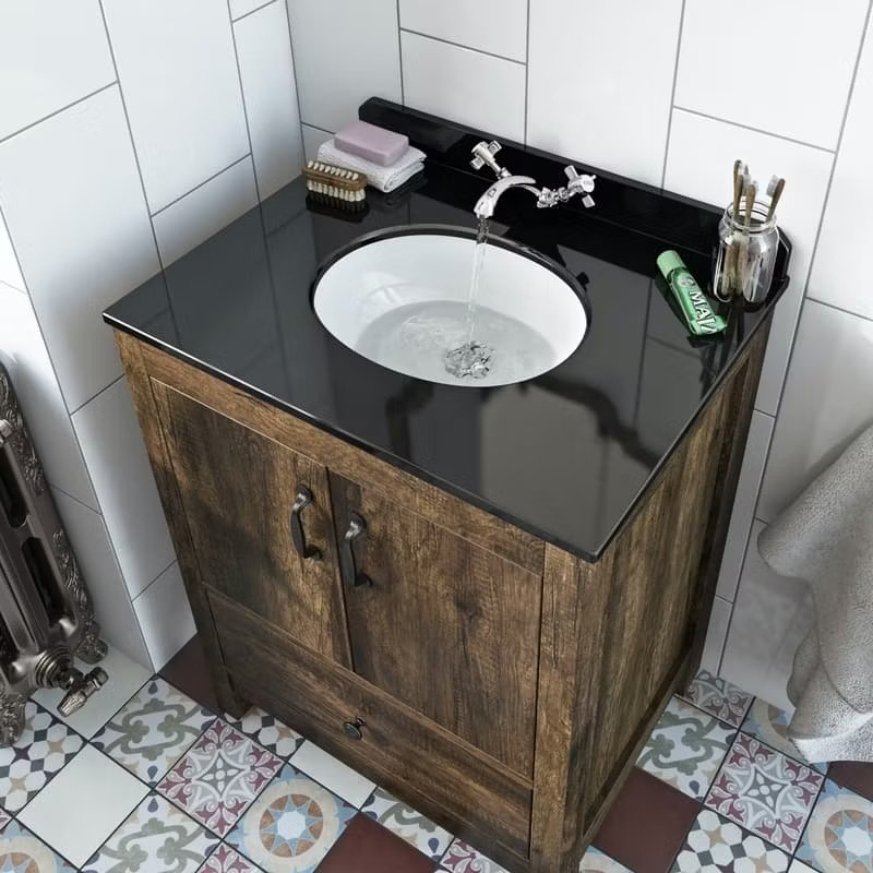 Rustic bathroom vanity unit with a sleek black countertop and traditional taps. The wooden cabinet contrasts beautifully with patterned floor tiles for a cosy, country-style look.