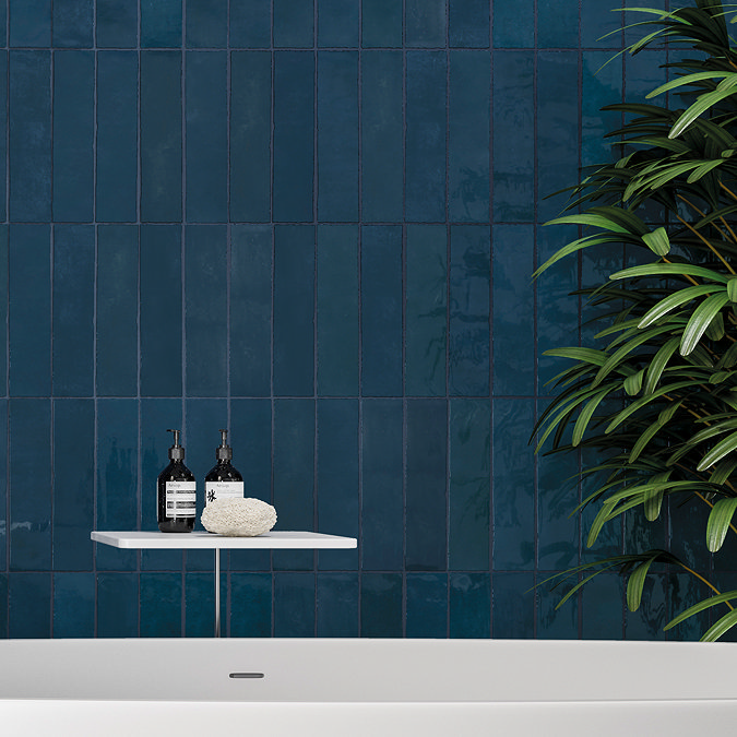 Deep blue vertical subway tiles in a modern bathroom with a white tub and minimalist decor.