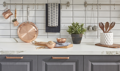 Modern kitchen counter with copper pans, potted plant, wooden utensils, and white subway tile backsplash