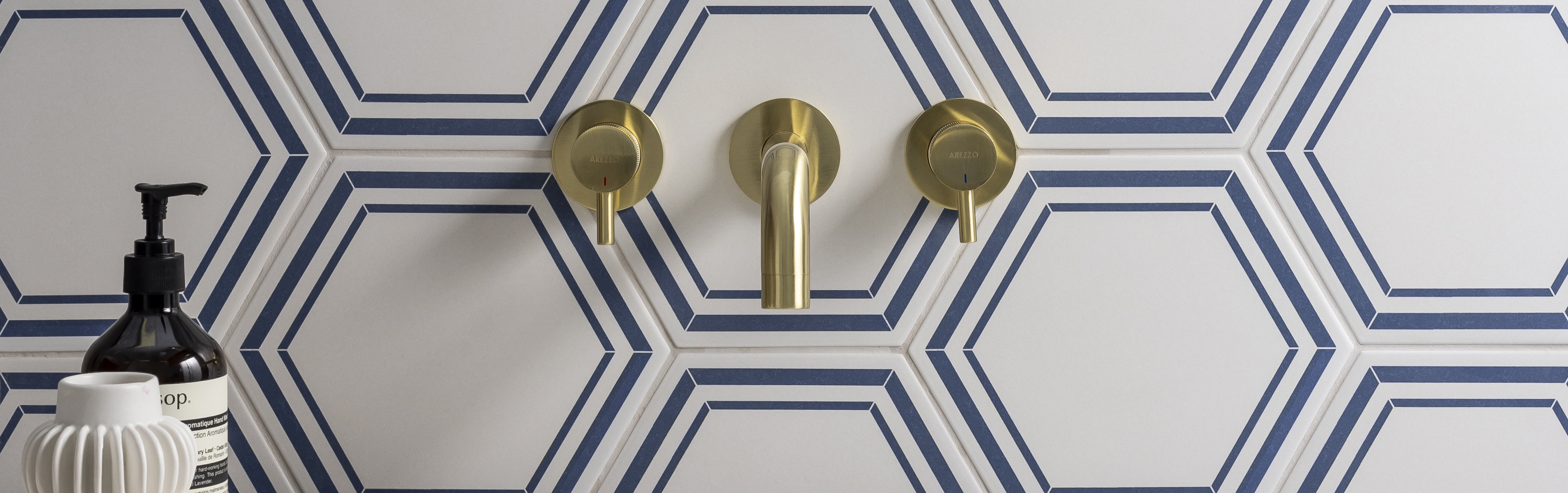 Wall-mounted brass bathroom taps set against bold hexagonal blue-and-white tiles, creating a modern geometric design