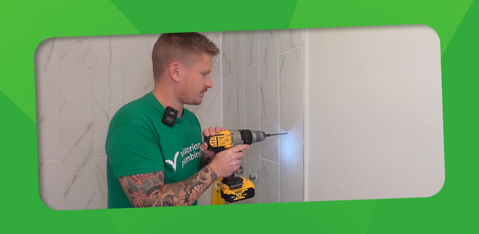 Victorian Plumbing expert demonstrating how to drill through a bathroom tile using a DeWalt drill with a diamond bit.