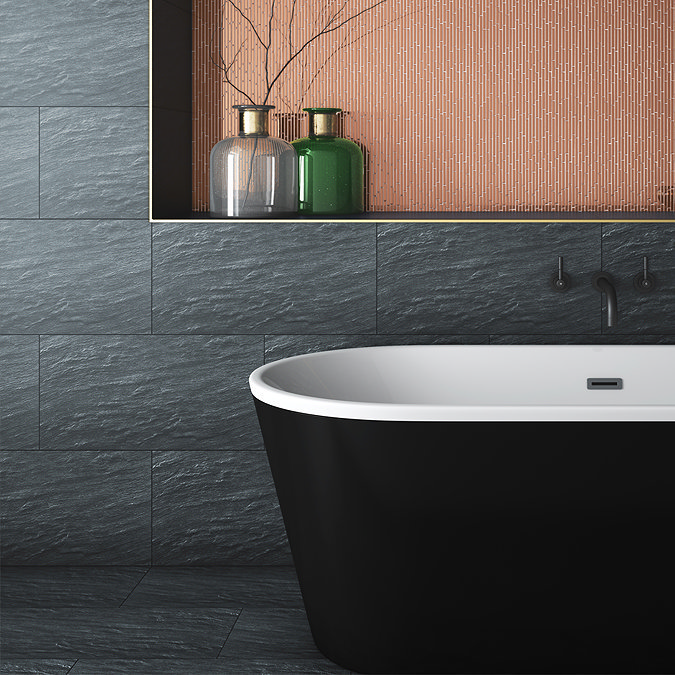 Modern bathroom with black textured slate wall tiles and a freestanding black and white bathtub, complemented by a copper mosaic feature wall and decorative glass vases.