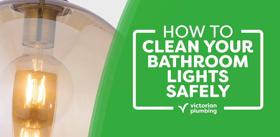 Close-up of a glowing vintage-style bulb in a bathroom light fixture with text overlay reading “How to Clean Your Bathroom Lights Safely” by Victorian Plumbing on a green background.