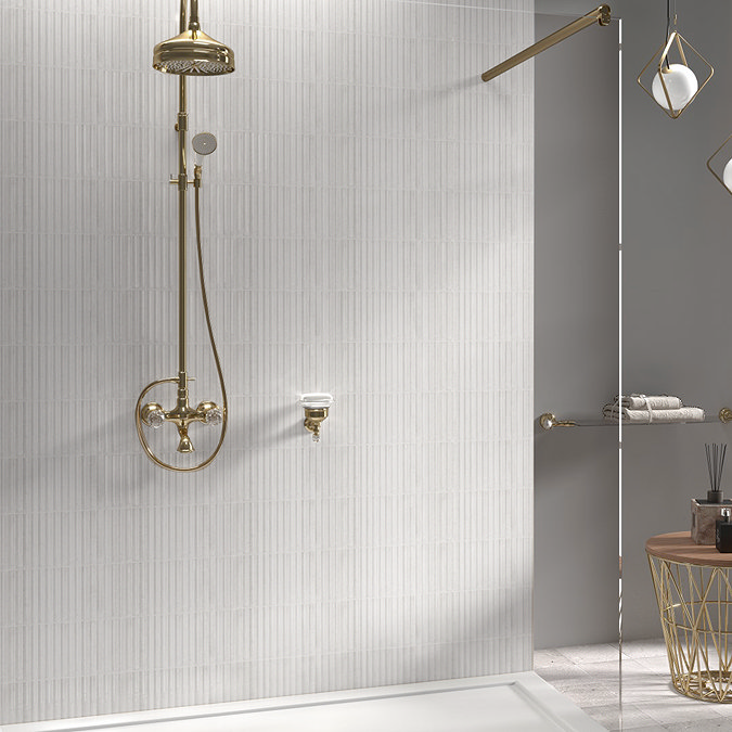 Elegant wet room featuring a gold vintage-style shower set against soft vertical striped white wall tiles. A sleek glass shower screen adds a modern touch, while a nearby wooden table holds bathroom essentials, blending luxury with minimalist design.