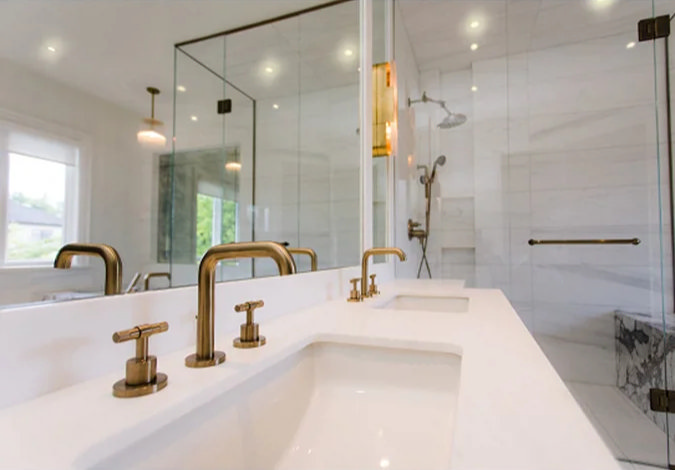 Elegant bathroom featuring a double sink vanity with brushed gold faucets, a frameless glass shower enclosure, and a white marble interior with modern lighting.