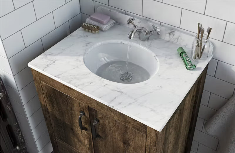 Bathroom vanity with a marble countertop and rustic wooden cabinet, blending luxury and natural textures with a chrome faucet and white tiled backdrop.
