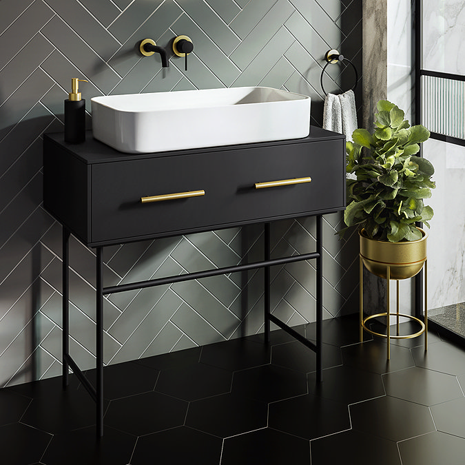 Modern black vanity unit with gold handles and a white vessel sink against herringbone wall tiles in a stylish bathroom