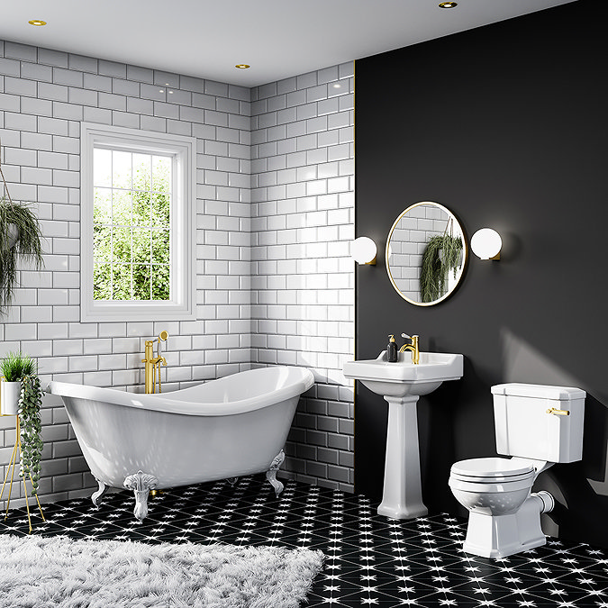 Stylish bathroom with a freestanding clawfoot bathtub, pedestal sink, and traditional toilet, all featuring gold fixtures. The room has white subway tiles, a black accent wall, star-patterned floor tiles, and a round mirror with wall sconces.