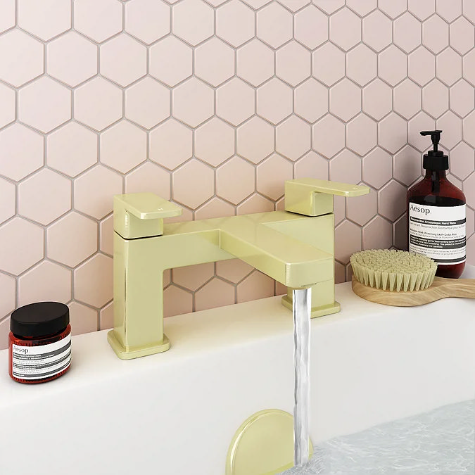 Modern yellow bath mixer tap with water flowing, set against a pastel pink hexagonal tile backdrop, accompanied by stylish bathroom essentials.