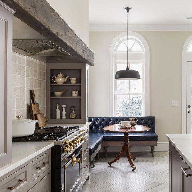 Elegant kitchen with rustic wood beam, black range cooker, built-in shelving, and cosy breakfast nook with navy tufted banquette