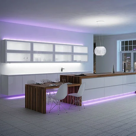 Modern kitchen with white cabinetry, wooden accents, and integrated purple LED strip lighting, creating an ambient glow. Features a built-in dining area with white chairs and a sparkling pendant light, set against a cityscape view through large windows.