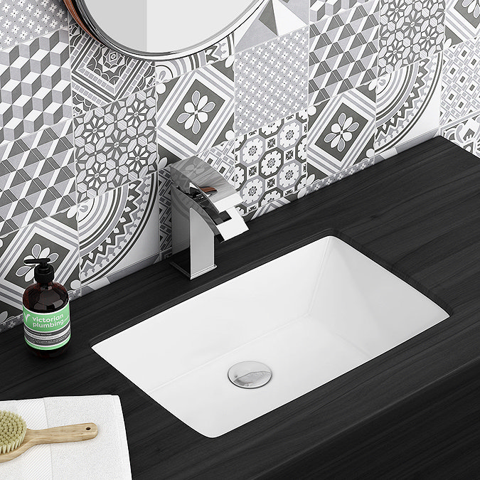 Undermounted white sink on dark wood countertop with chrome tap and geometric patterned tiles in a modern bathroom