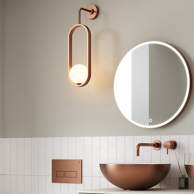 Elegant bathroom with a copper-toned oval wall light, a matching round illuminated mirror, and a copper vessel sink with a minimalist wall-mounted tap, complemented by white subway tiles.