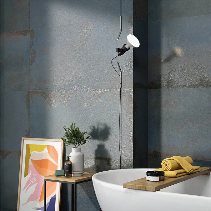 Textured blue wall tiles in a contemporary bathroom with a freestanding white tub, modern pendant light, and wooden side table with decor.