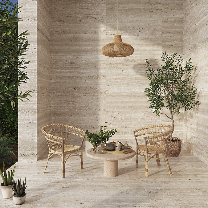 Travertine-effect floor and wall tiles in a cosy outdoor patio with wicker chairs, a round table, potted plants, and natural decor for a warm, inviting atmosphere.