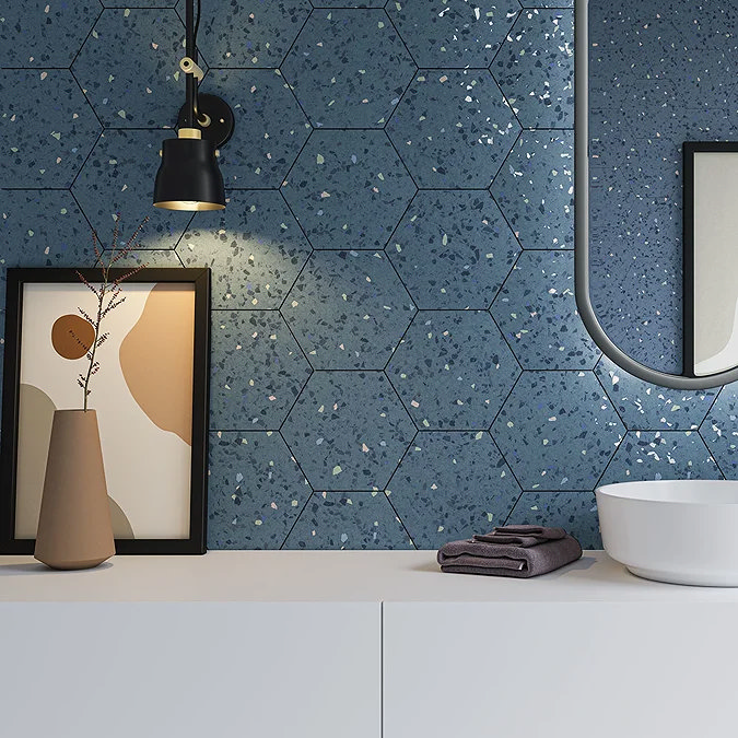 Modern bathroom with deep blue terrazzo hexagonal tiles, white bowl basin, black pendant light, and abstract framed artwork, styled with minimalistic decor and soft lighting.