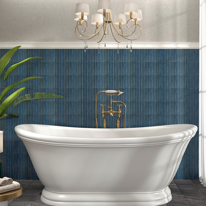 Luxury bathroom featuring a white freestanding statement bathtub against a sapphire blue textured tile wall, with gold brass fittings, a chandelier, and a large leafy plant for added elegance.