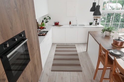 Bright modern kitchen with white cabinets, wooden breakfast bar, striped rug, and large window letting in natural light