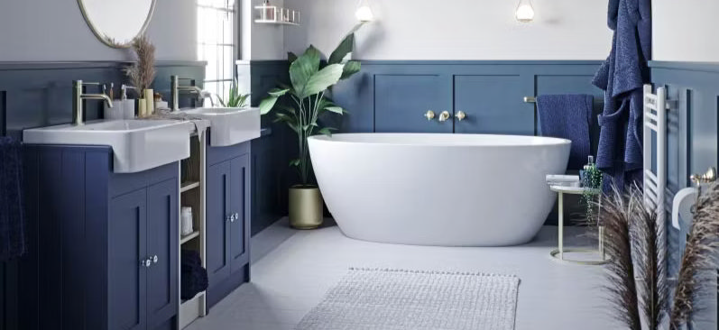 Modern bathroom with blue wood panelling, freestanding white bathtub, and twin sinks. Features elegant lighting, indoor plants, and gold fixtures for a stylish finish