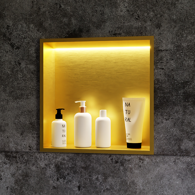 Illuminated recessed bathroom niche with a golden interior, showcasing sleek white toiletry bottles and a tube against a textured dark grey tile wall, creating a luxurious and modern look.