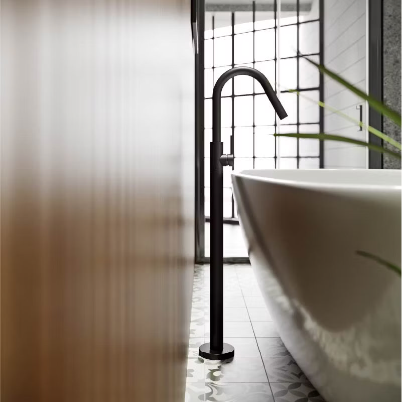 lose-up of a freestanding black bath tap next to a white bathtub, featuring a patterned tile floor and large industrial-style windows, creating a modern soft industrial bathroom aesthetic.