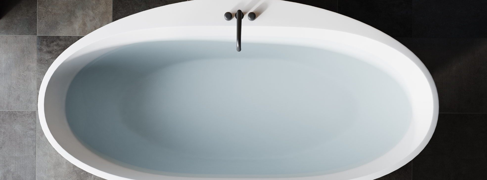 Overhead view of a white steel enamel bath filled with water, set against modern grey floor tiles with a matte black tap — showcasing a sleek, contemporary bathroom finish.
