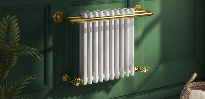 Traditional white column radiator with brass towel rail mounted on a dark green panelled wall