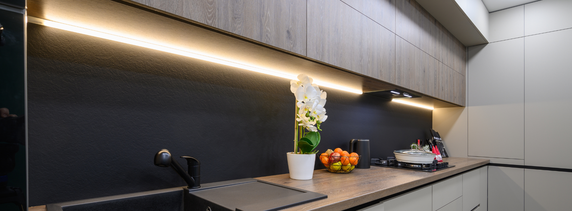 Warm white LED under-cabinet strip lighting illuminating wood worktops in a modern kitchen with matt black tap and flat-panel cupboards