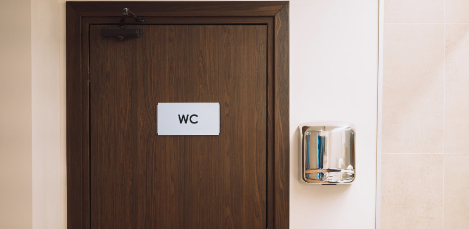 WC sign on a wooden toilet door in a public restroom, showing the water closet abbreviation.