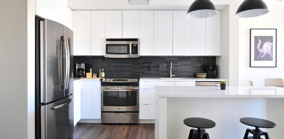 Modern white kitchen with stainless steel appliances, black tile backsplash, and breakfast bar with stools