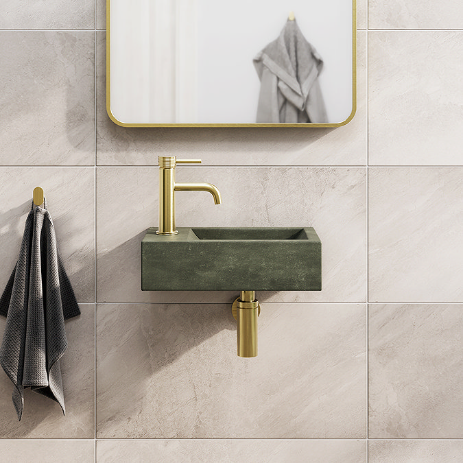 Minimalist bathroom featuring a dark green freestanding wall-mounted sink with brushed brass tap and matching hardware against a natural stone tile backdrop.