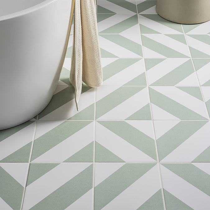 Green and white geometric pattern floor tiles in a bathroom with a white bathtub and a beige towel for a fresh, modern look.