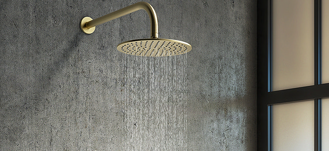 Modern brass rainfall shower head with water flowing, set against a textured wall